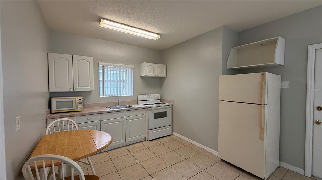 A kitchen features white cabinets, a white stove, a refrigerator, and a small wooden table — 627 ORCHID DRIVE, DAVENPORT, FL