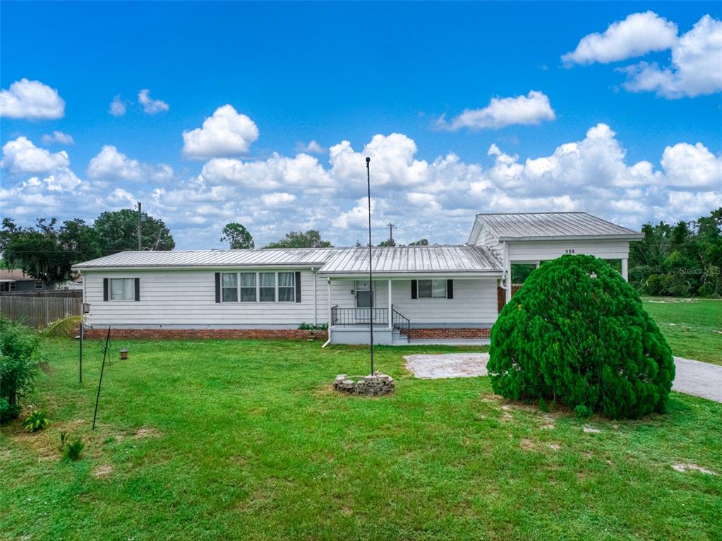 A single-story white house with a metal roof and a large green bush in front — 906 WHATLEY COURT, SEBRING, FL