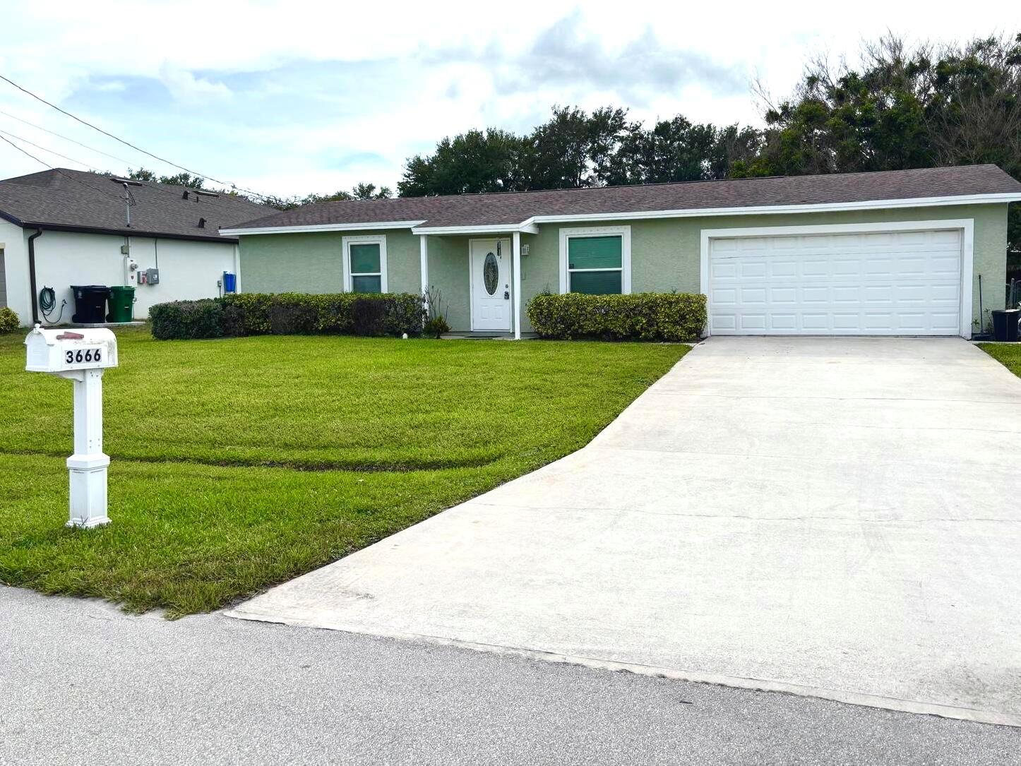 A single-story house with light green siding, a white garage door, and a front lawn — 3666 SW Rivera Street, FL 34953, FL