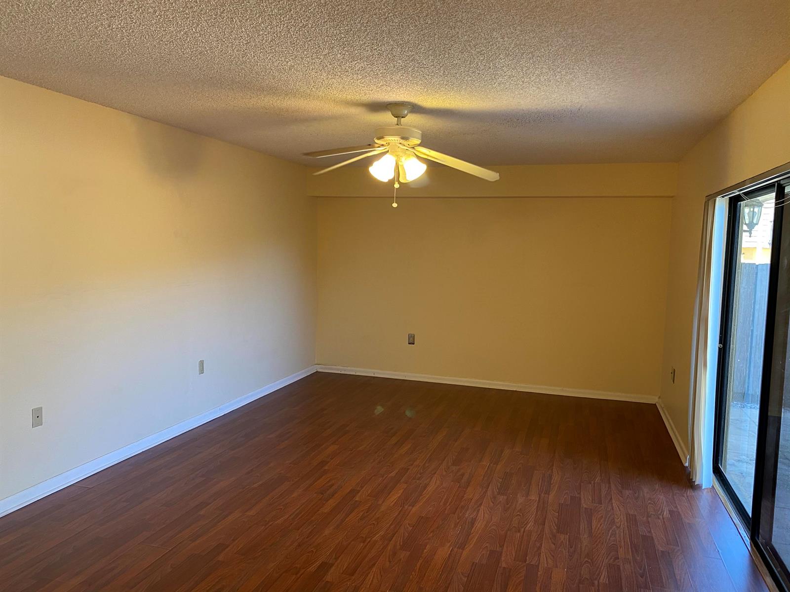 An empty room with yellow walls, wood-look flooring, a ceiling fan, and sliding glass doors — 1603 16th Way, West Palm Beach FL 33407, WEST PALM BEACH, FL