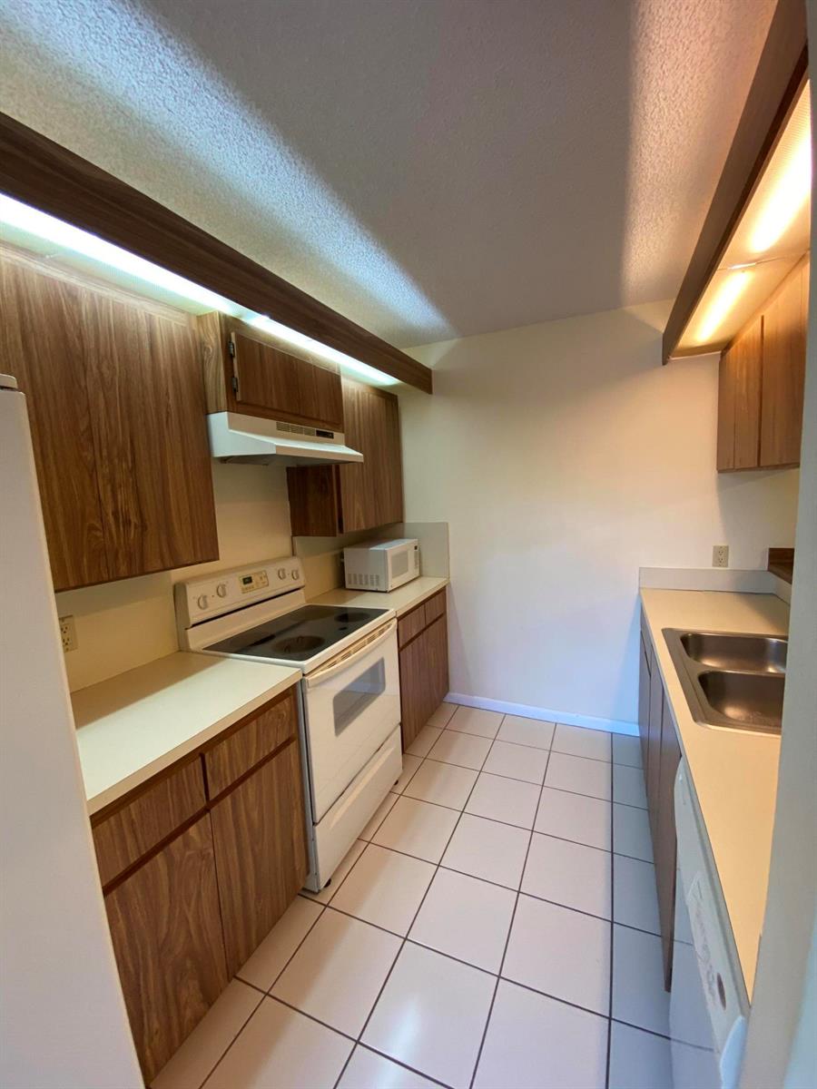 A galley kitchen features wood-grain cabinets, white appliances, a tiled floor, and under-cabinet lighting — 1603 16th Way, West Palm Beach FL 33407, WEST PALM BEACH, FL