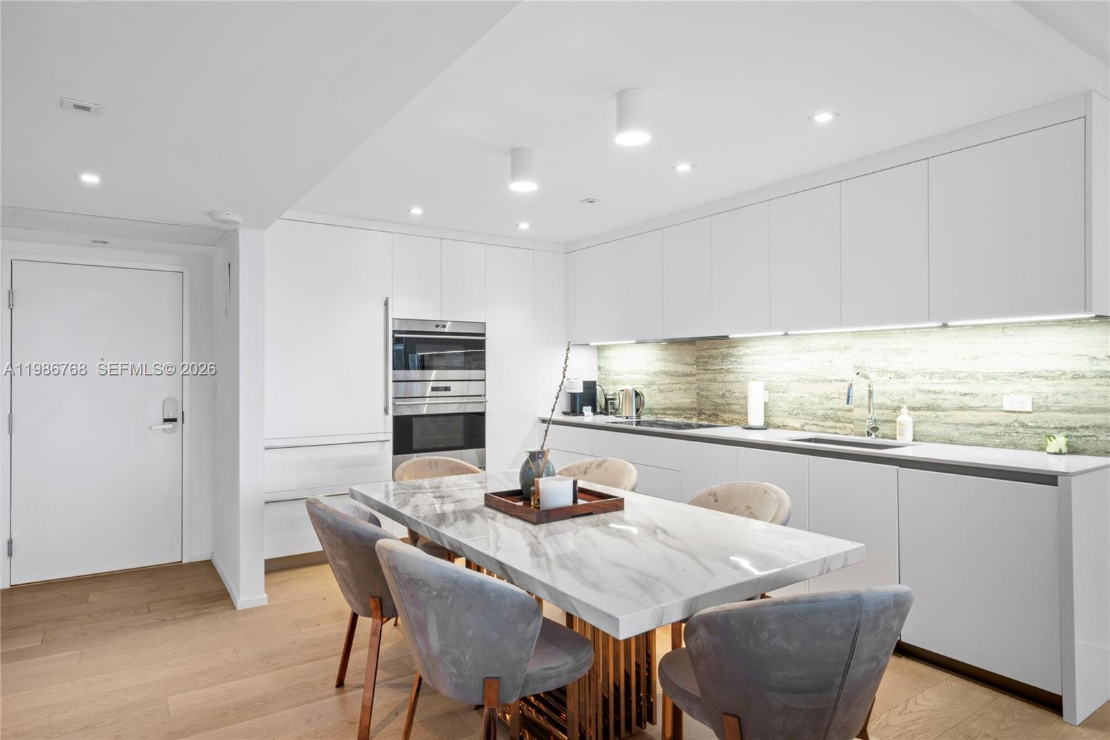 A modern kitchen features white cabinetry, a marble dining table, and light wood flooring — 2301 Collins Ave # 624, Miami Beach FL 33139, MIAMI BEACH, FL