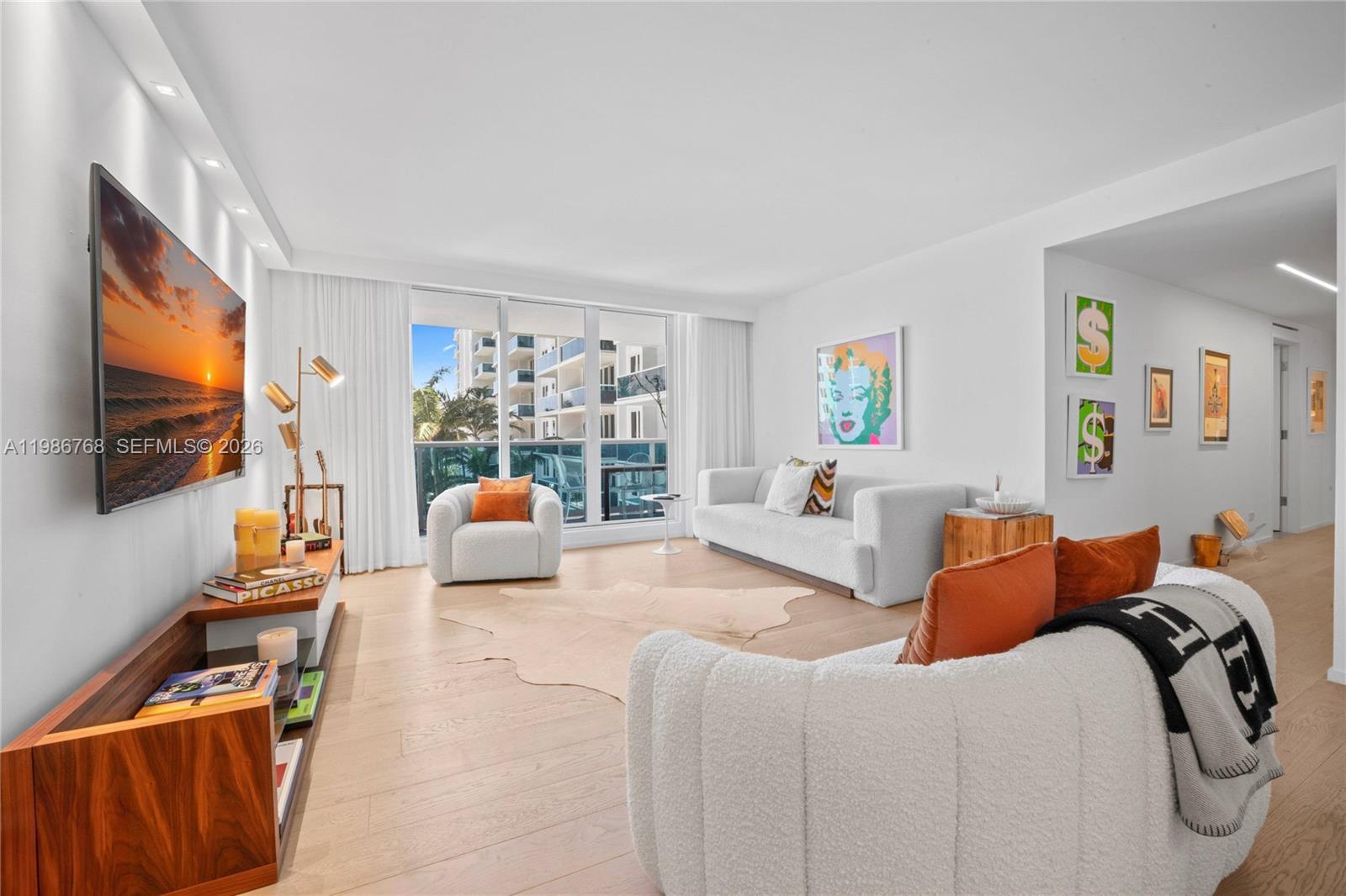 A bright living room features white furniture, a wooden media console, and a balcony view — 2301 Collins Ave # 624, Miami Beach FL 33139, MIAMI BEACH, FL