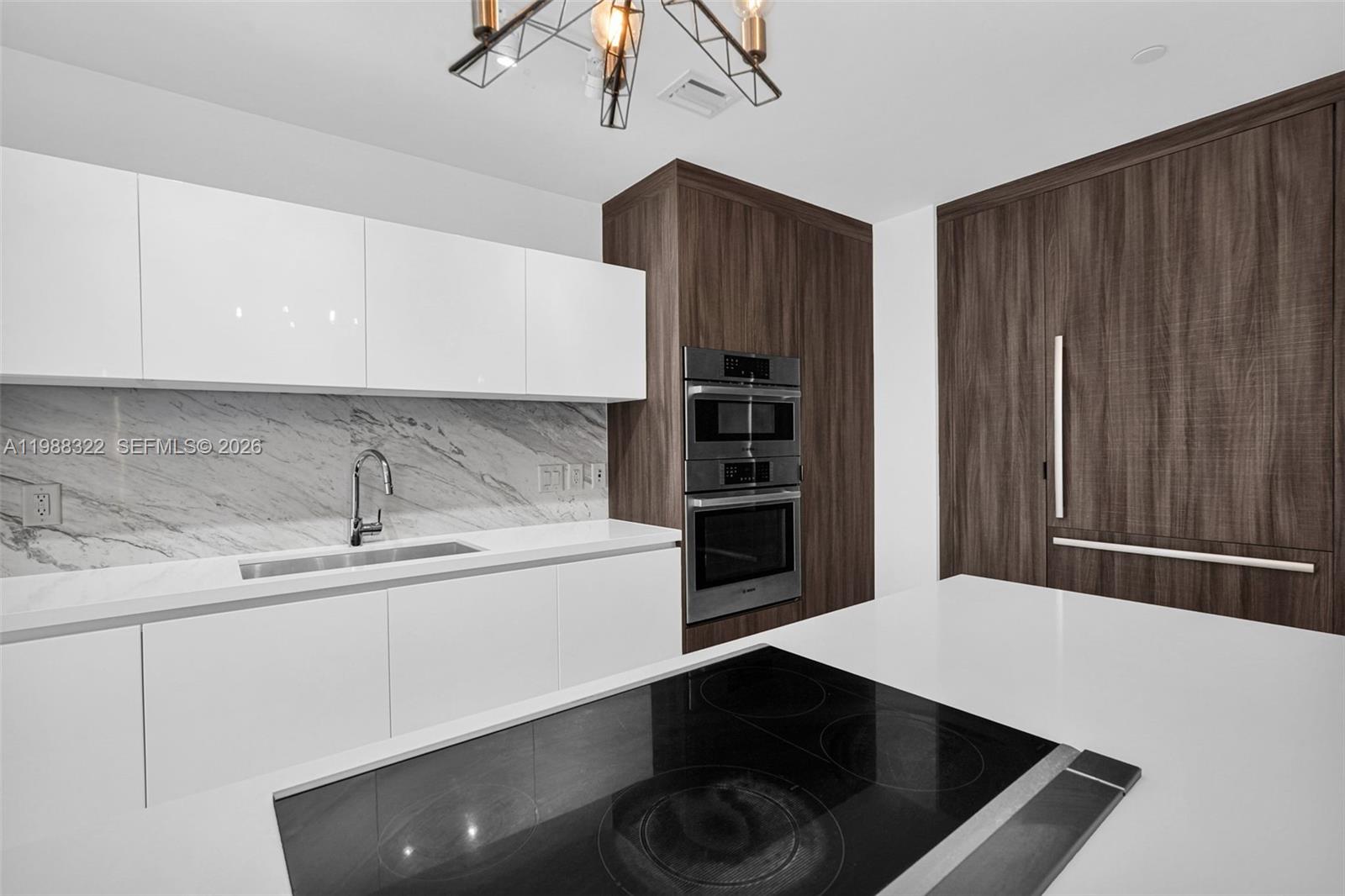 A modern kitchen features white cabinetry, marble-patterned backsplashes, dark wood paneling, and stainless appliances — 851 NE 1st Ave # 2912, Miami FL 33132, MIAMI, FL