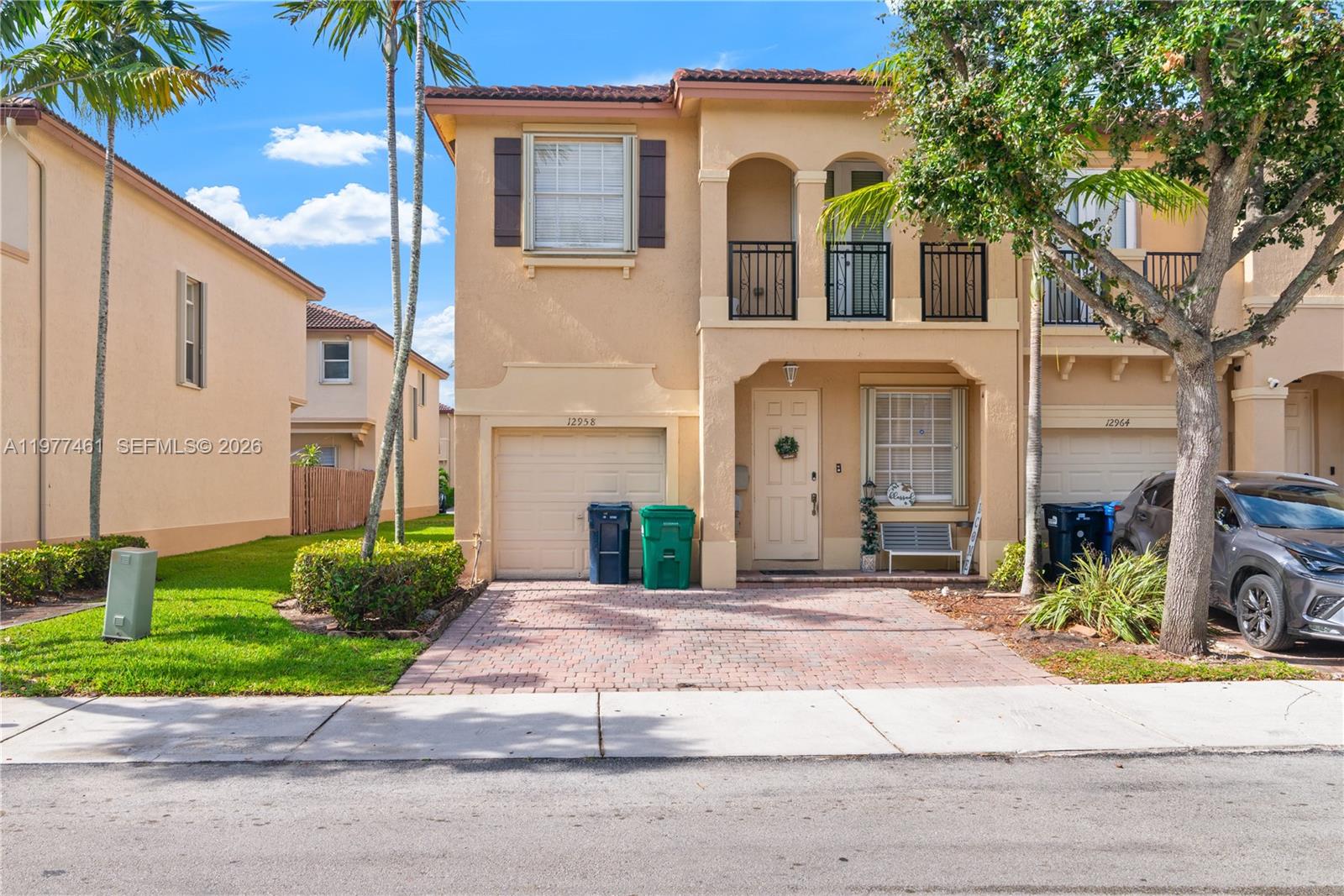 A two-story tan stucco townhouse features a brick driveway, a garage, and a front balcony — 12958 SW 135th St, Miami FL 33186, MIAMI, FL
