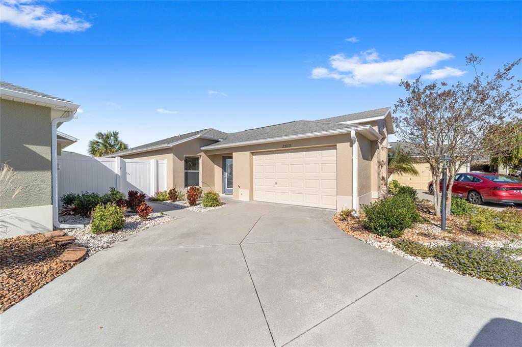 A tan single-story house features a two-car garage, a concrete driveway, and landscaped front yard — 2303 NAUTILUS LANE, THE VILLAGES, FL
