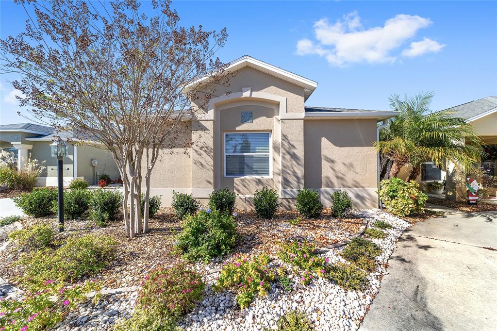 A beige stucco house exterior features a gray front door with a glass insert — 2303 NAUTILUS LANE, THE VILLAGES, FL