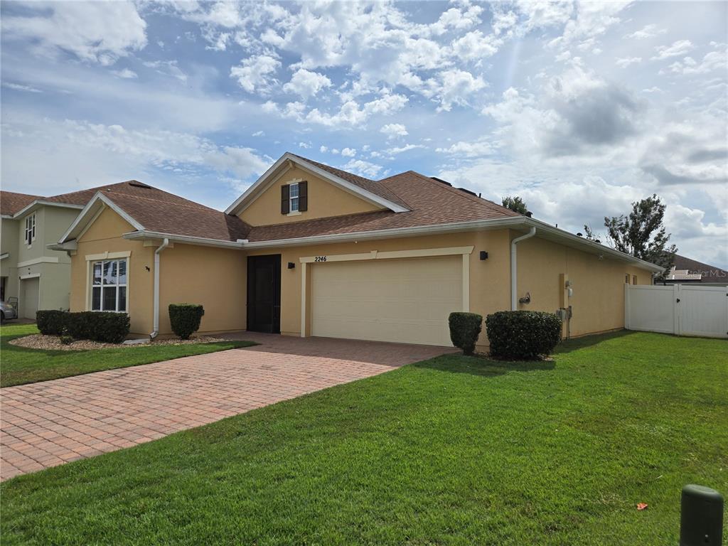 A single-story house with a tan stucco exterior, a two-car garage, and a brick driveway — 2246 WAUKEGAN DRIVE, KISSIMMEE, FL