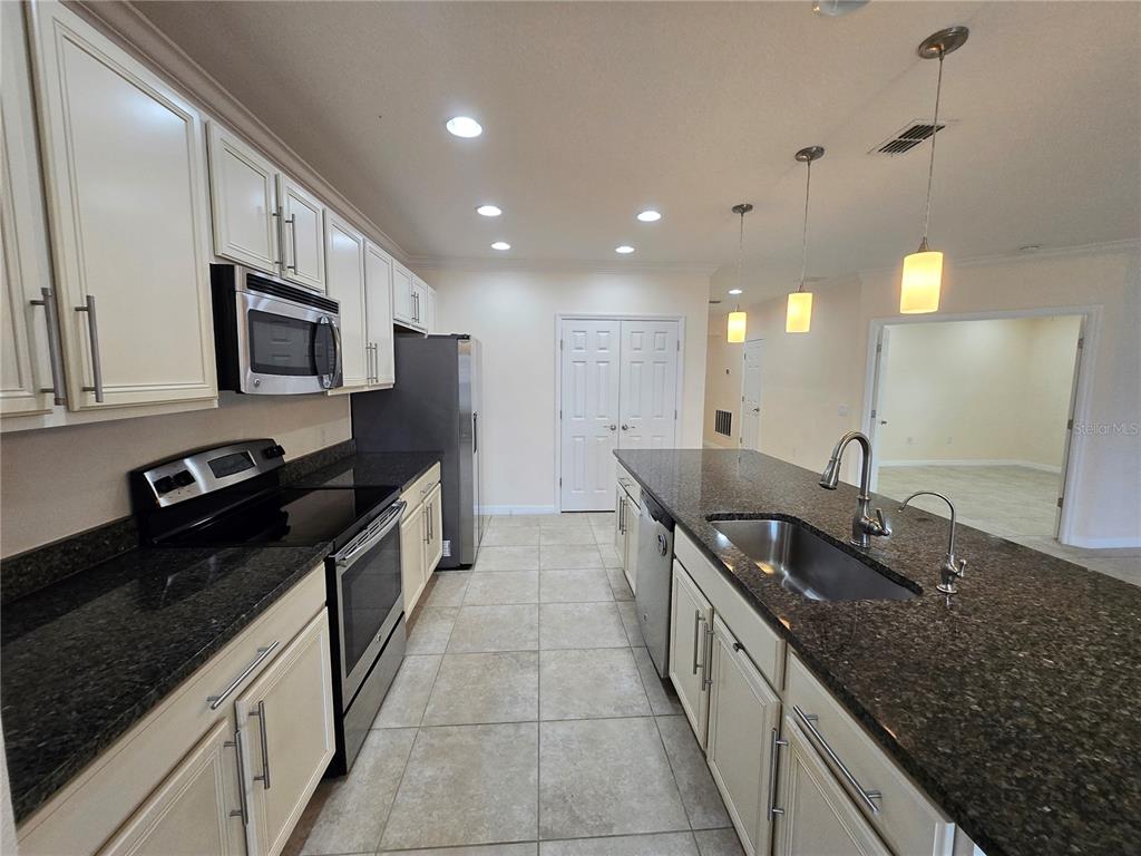A kitchen features white cabinets, dark granite countertops, stainless steel appliances, and a central island — 2246 WAUKEGAN DRIVE, KISSIMMEE, FL