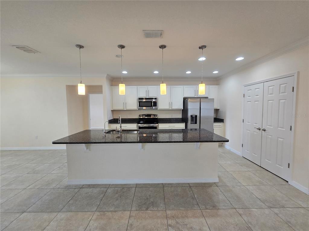 A kitchen with a granite-topped island, white cabinetry, stainless steel appliances, and tile flooring — 2246 WAUKEGAN DRIVE, KISSIMMEE, FL