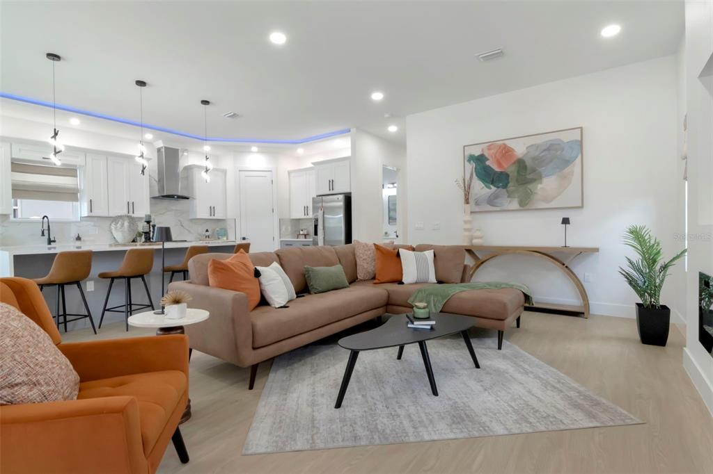 A modern open-concept living room features a brown sectional sofa, orange armchair, and kitchen island — 5009 9TH AVENUE S, GULFPORT, FL