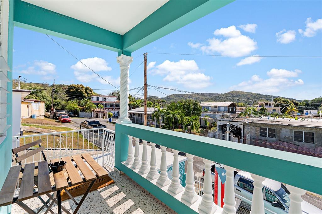 A balcony with a turquoise railing and white balusters overlooks a neighborhood with distant hills — Solar 124 CALLE 4, YAUCO, PR