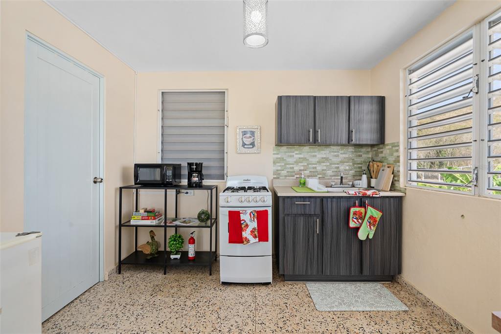 A small kitchen features dark wood cabinets, a white stove, and a metal shelving unit — Solar 124 CALLE 4, YAUCO, PR