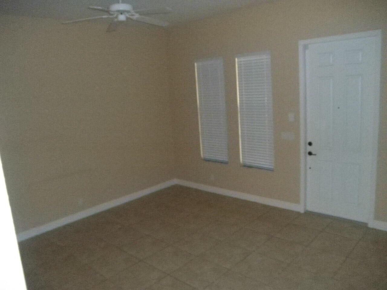 An empty room with tan walls, tile flooring, a ceiling fan, and a white door — BOCA RATON, FL