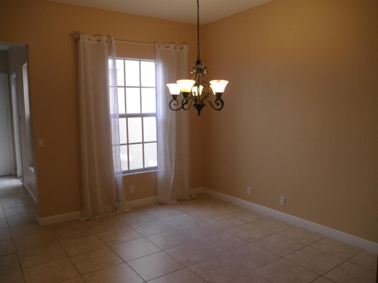 A dining room with tan walls, tile flooring, a window with white curtains, and a chandelier — BOCA RATON, FL