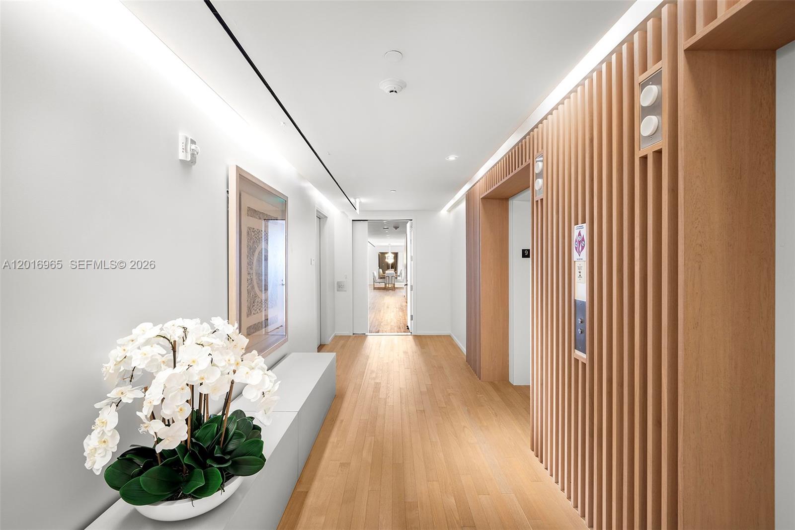 A hallway features light wood flooring, vertical wood slat wall paneling, and a white orchid — 2901 Collins Ave # 901, Miami Beach FL 33140, MIAMI BEACH, FL