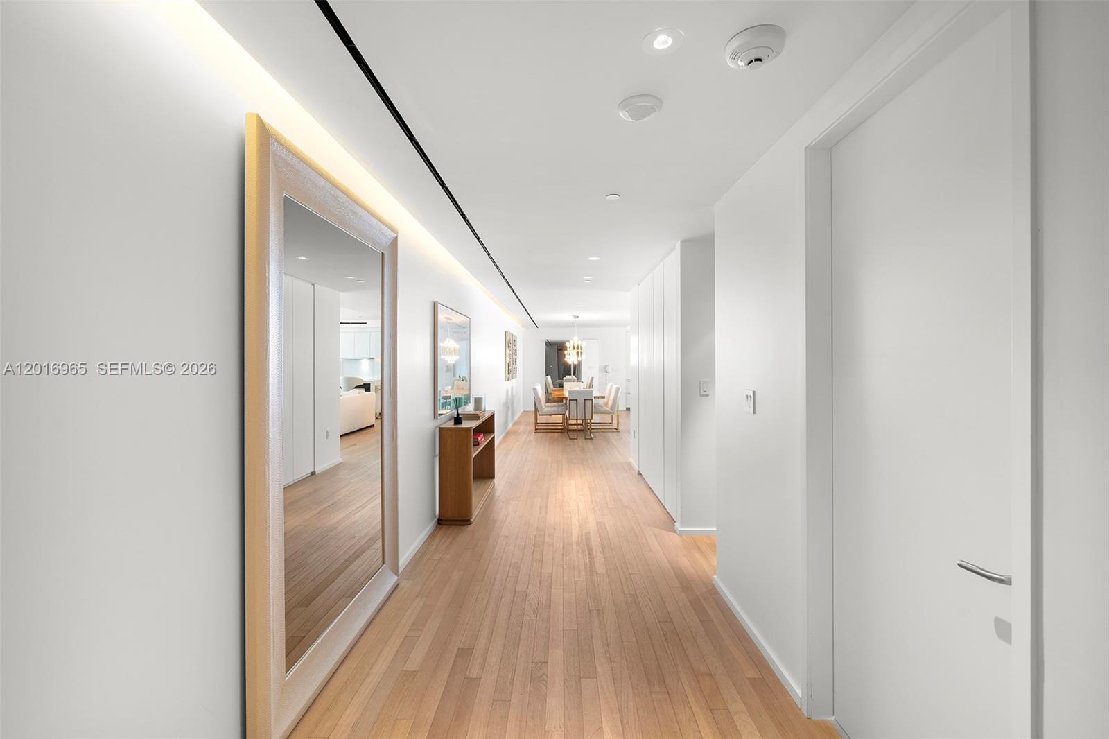 A long hallway with light wood flooring leads to a dining area with a chandelier — 2901 Collins Ave # 901, Miami Beach FL 33140, MIAMI BEACH, FL
