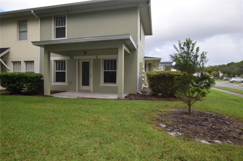 A two-story building features a covered concrete patio, green lawn, and a small tree — 9796 TIVOLI VILLA DRIVE, ORLANDO, FL