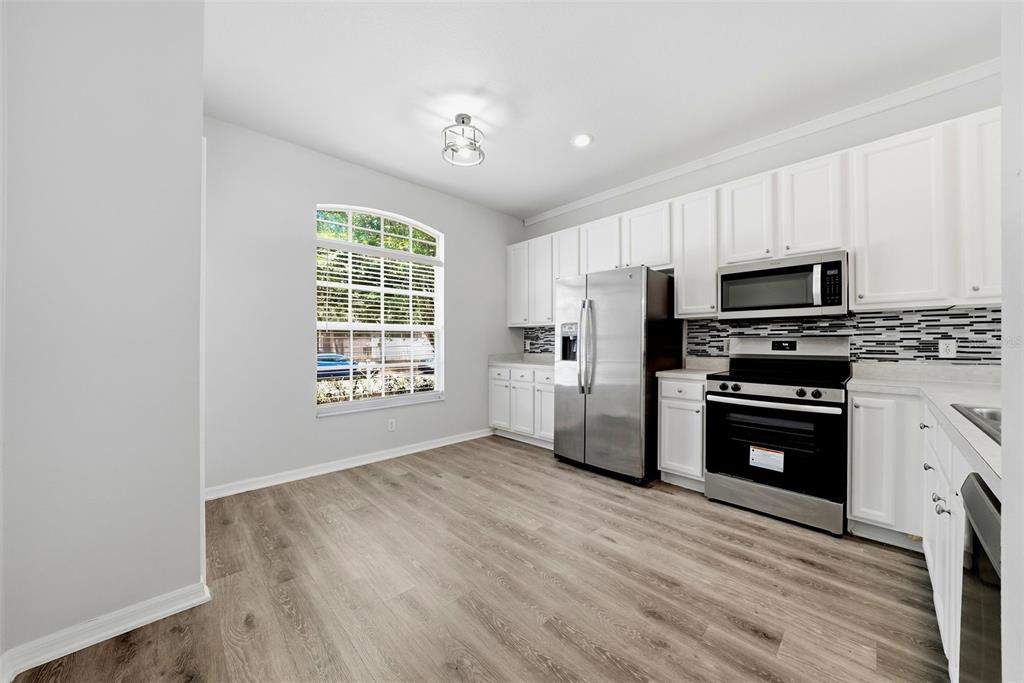 A kitchen with white cabinets, stainless steel appliances, and wood-look flooring under a window — 403 LAGUNA MILL DRIVE, RUSKIN, FL