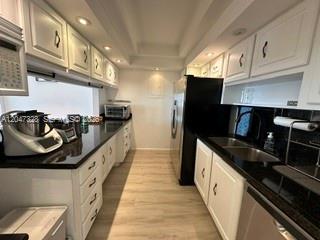 A galley kitchen features white cabinets, black countertops, and light wood-look flooring — 199 Ocean Lane Dr # 903, Key Biscayne FL 33149, KEY BISCAYNE, FL