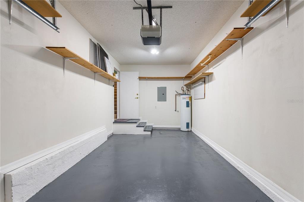 An empty garage features gray painted floors, white walls, wooden wall-mounted shelves, and a water heater — 5999 LAKE POINTE DRIVE UNIT 608, ORLANDO, FL