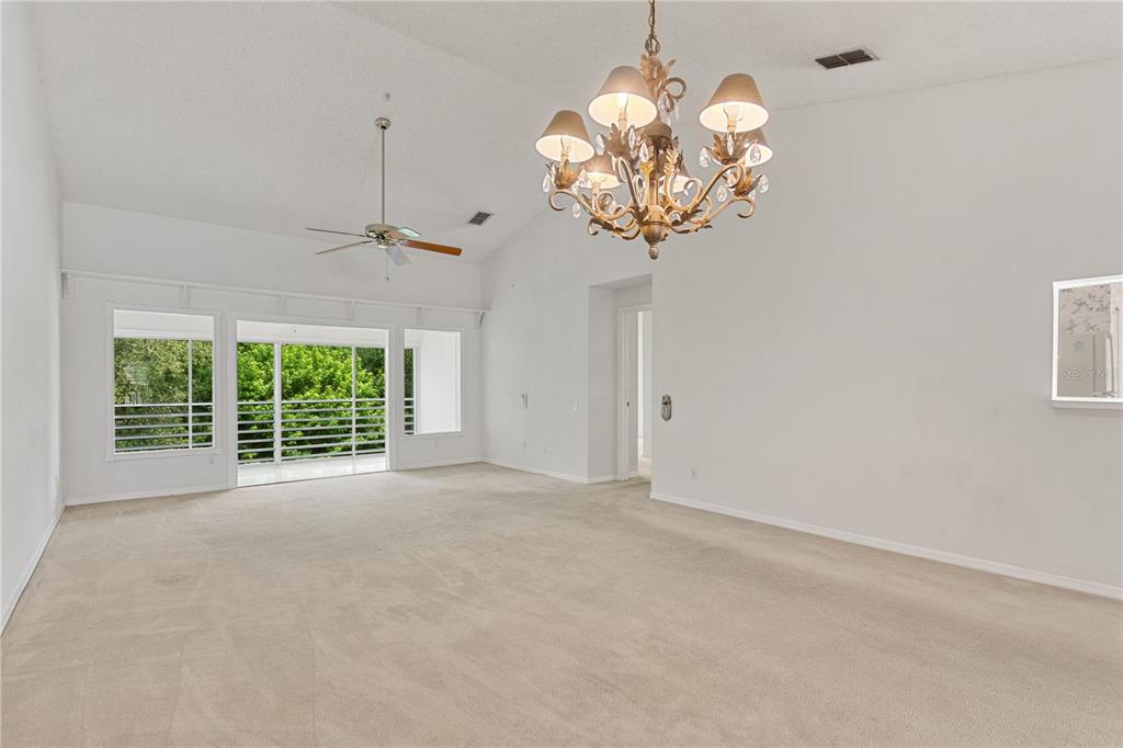 A spacious living room features vaulted ceilings, beige carpeting, a chandelier, and a ceiling fan — 5999 LAKE POINTE DRIVE UNIT 608, ORLANDO, FL