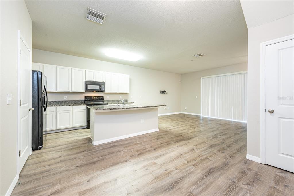 A kitchen with white cabinets, granite countertops, and black appliances opens to a living area — 8908 INDIGO TRAIL LOOP, RIVERVIEW, FL