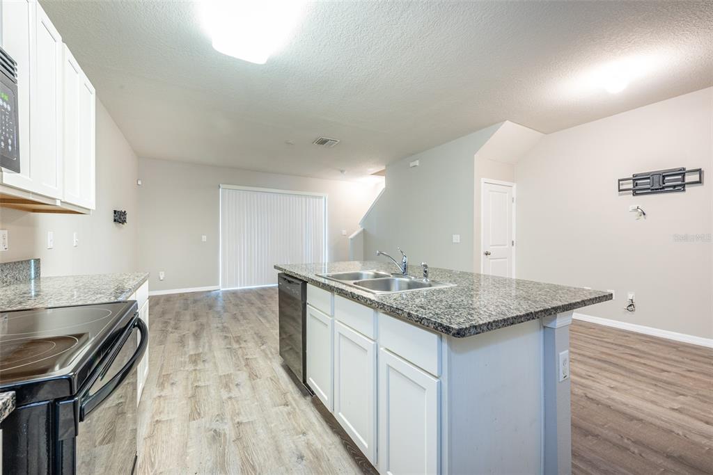 A kitchen with white cabinets, granite countertops, and a center island overlooks an open living area — 8908 INDIGO TRAIL LOOP, RIVERVIEW, FL