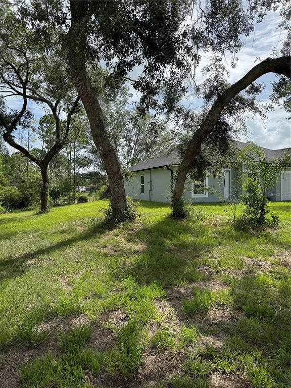 A gray house sits behind large trees on a grassy, sloped lot — 1780 CONVERSE COURT, DELTONA, FL