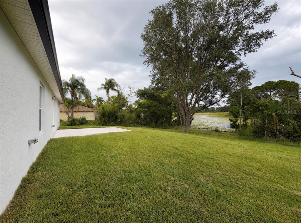 A grassy backyard features a concrete patio next to a house and a pond view — 1780 CONVERSE COURT, DELTONA, FL