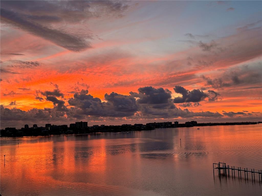 A vibrant sunset glows over a calm body of water with a distant city skyline — 920 N OSCEOLA AVENUE UNIT 702, CLEARWATER, FL