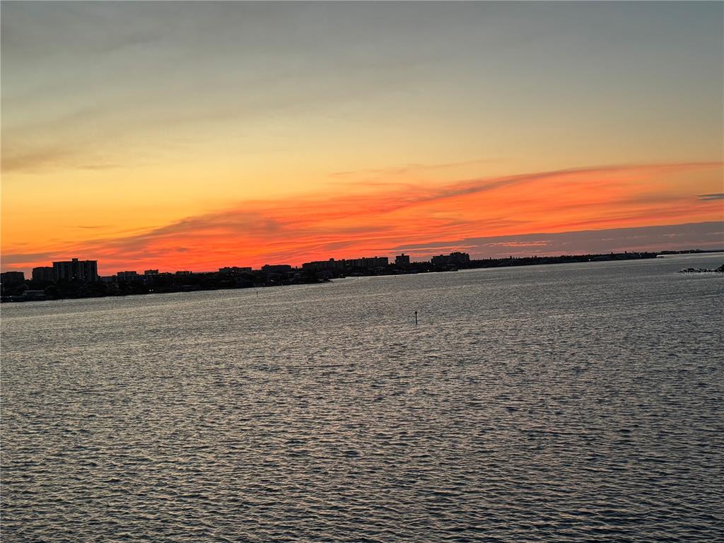 A vibrant sunset glows over a body of water with a distant city skyline — 920 N OSCEOLA AVENUE UNIT 702, CLEARWATER, FL