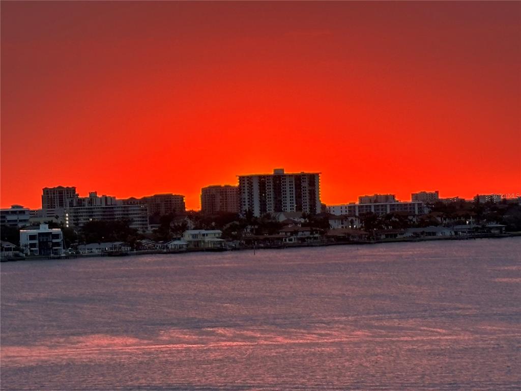 A vibrant red sunset glows behind a skyline of waterfront buildings and a calm bay — 920 N OSCEOLA AVENUE UNIT 702, CLEARWATER, FL