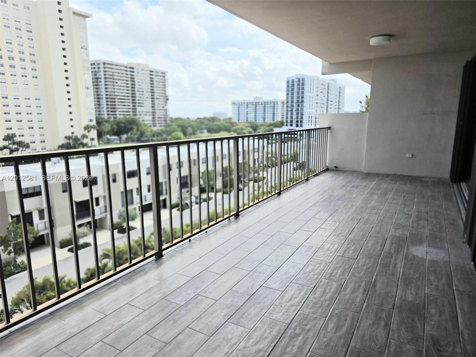 A spacious balcony features wood-look tile flooring and a metal railing overlooking urban buildings — 1800 NE 114th St # 706, Miami FL 33181, MIAMI, FL