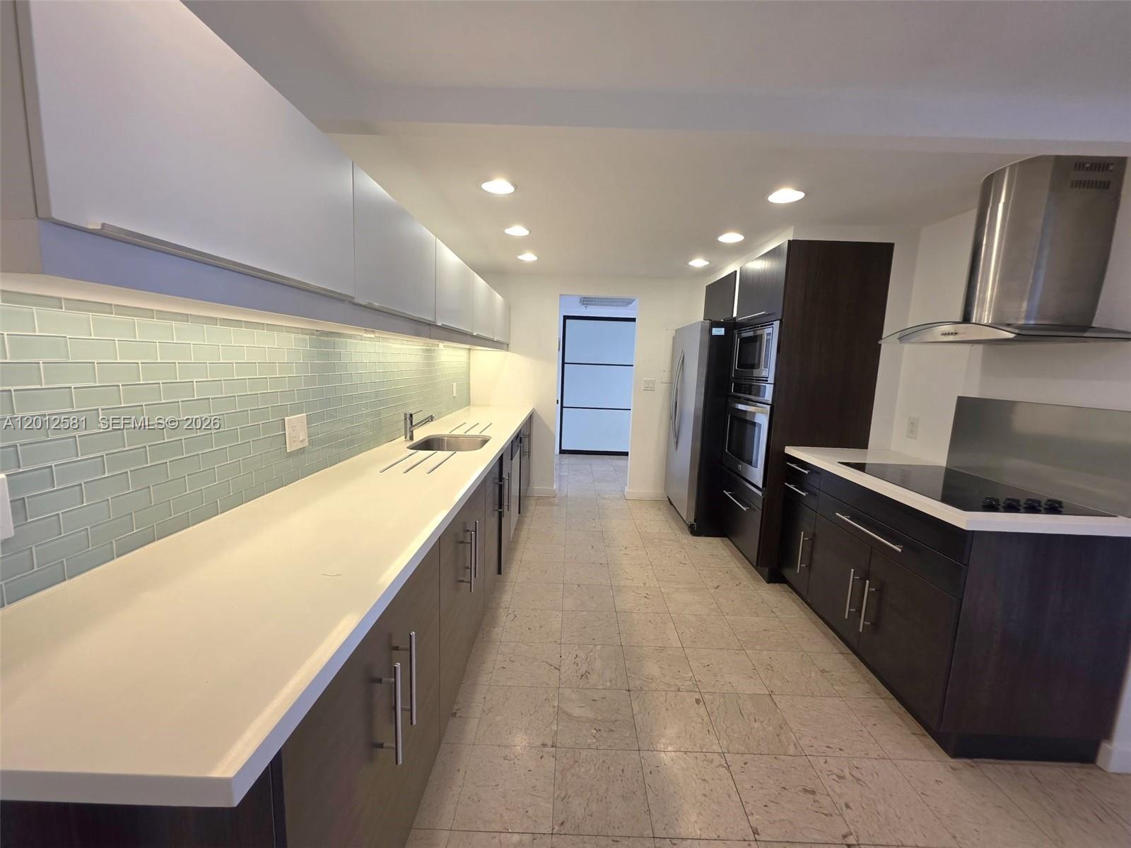 A modern kitchen features dark wood cabinets, white countertops, and a light blue tiled backsplash — 1800 NE 114th St # 706, Miami FL 33181, MIAMI, FL