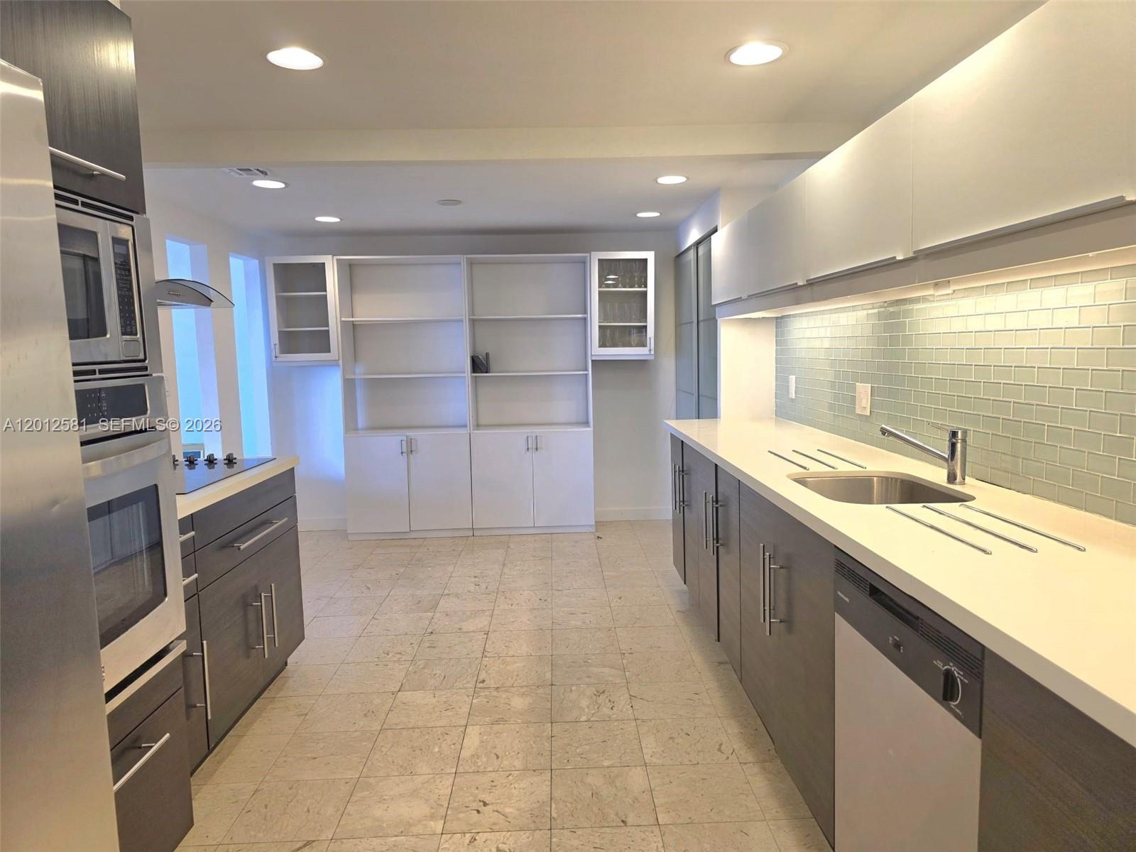 A modern kitchen features dark wood cabinets, white countertops, and a light blue tiled backsplash — 1800 NE 114th St # 706, Miami FL 33181, MIAMI, FL