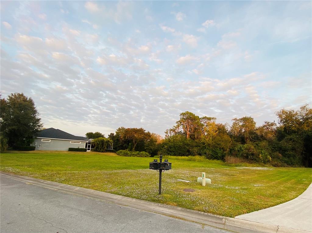 A vacant grassy corner lot sits next to a house under a cloudy sky — 617 130TH COURT NE, BRADENTON, FL