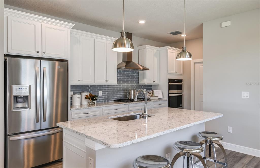 A modern kitchen features white cabinets, a granite island, stainless steel appliances, and gray backsplash — 5852 SW 86TH AVENUE ROAD, OCALA, FL