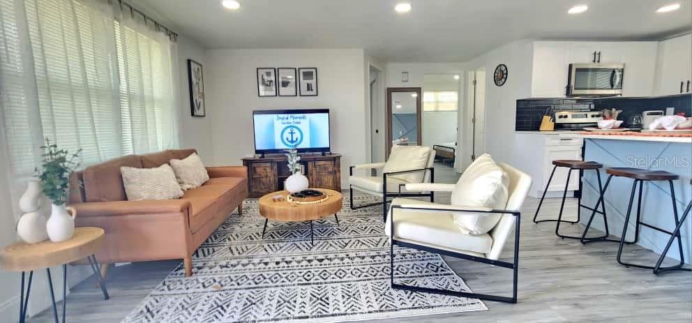 An open-concept living room features a tan sofa, two white armchairs, and a kitchen island — 4012 VALENCIA DRIVE, NEW PORT RICHEY, FL