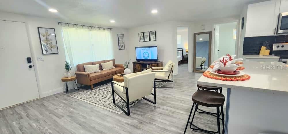 This open-concept living room features light wood-look flooring, a brown sofa, and a kitchen island — 4012 VALENCIA DRIVE, NEW PORT RICHEY, FL