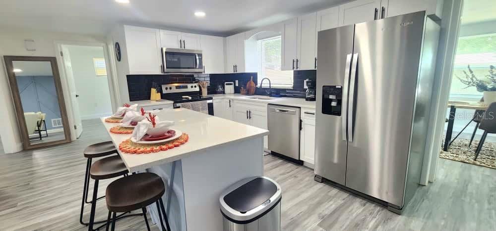 A modern kitchen features white cabinets, stainless steel appliances, a center island, and black backsplash — 4012 VALENCIA DRIVE, NEW PORT RICHEY, FL