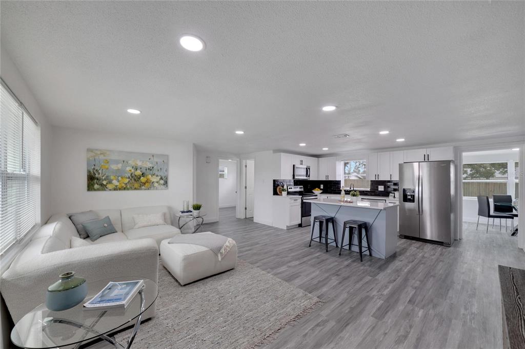 An open-concept living room and kitchen featuring white cabinetry, stainless steel appliances, and gray flooring — 4012 VALENCIA DRIVE, NEW PORT RICHEY, FL