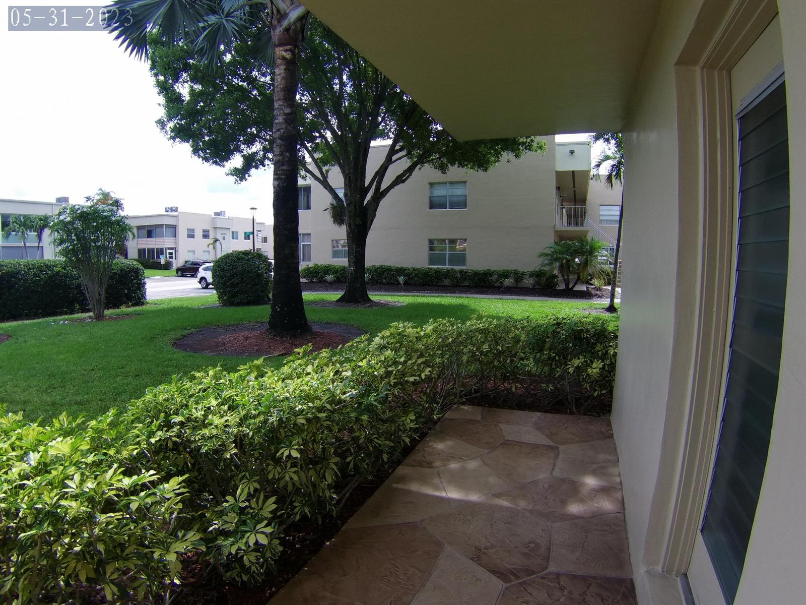 A view from a stone-paved patio looking out toward a grassy lawn and apartment buildings — 865 Flanders S, Delray Beach FL 33484, DELRAY BEACH, FL