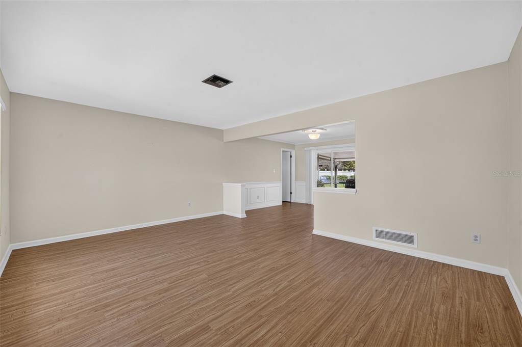 An empty living room features light-colored walls, wood-look flooring, and a partial wall divider — 125 E FAITH TERRACE, MAITLAND, FL