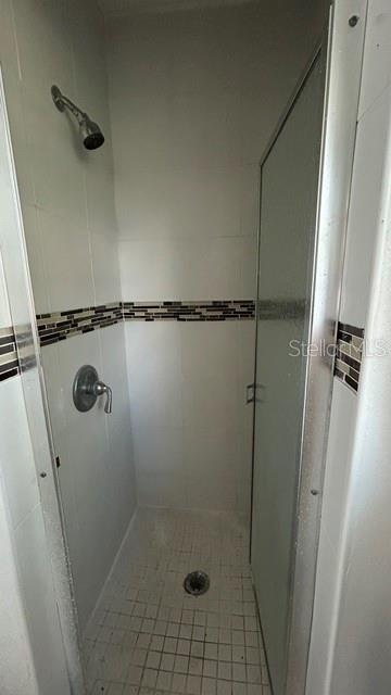 A walk-in shower features white tiled walls with a decorative brown accent stripe and glass doors — 2506 SANDY LANE, ORLANDO, FL