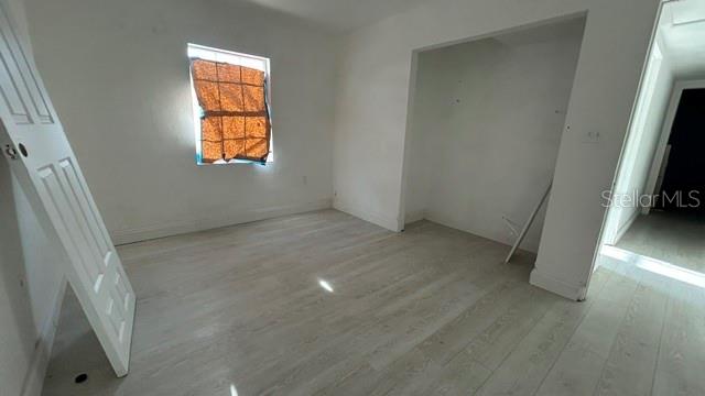 An empty room features light-colored wood-look flooring, white walls, and a window with orange covering — 2506 SANDY LANE, ORLANDO, FL