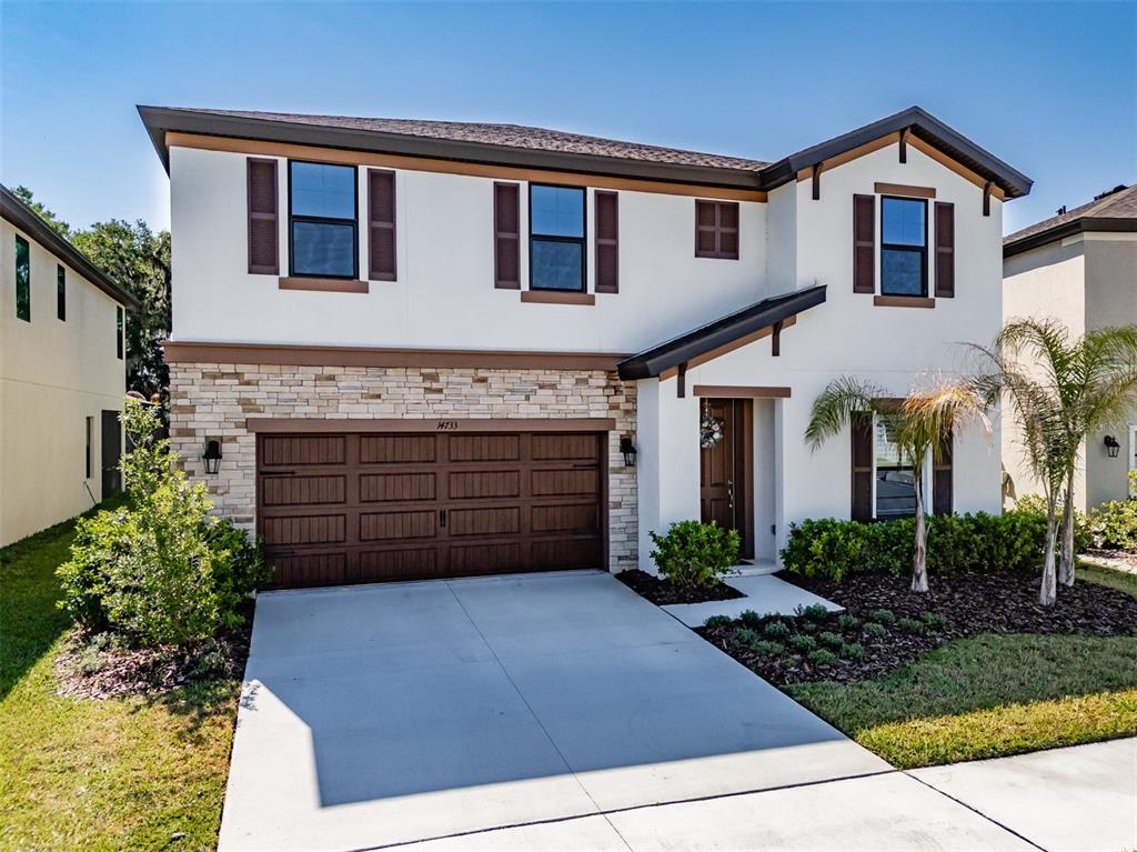 A two-story house with a white stucco facade, stone veneer, and a brown garage door — 14733 GALLOP RUN DRIVE, LITHIA, FL