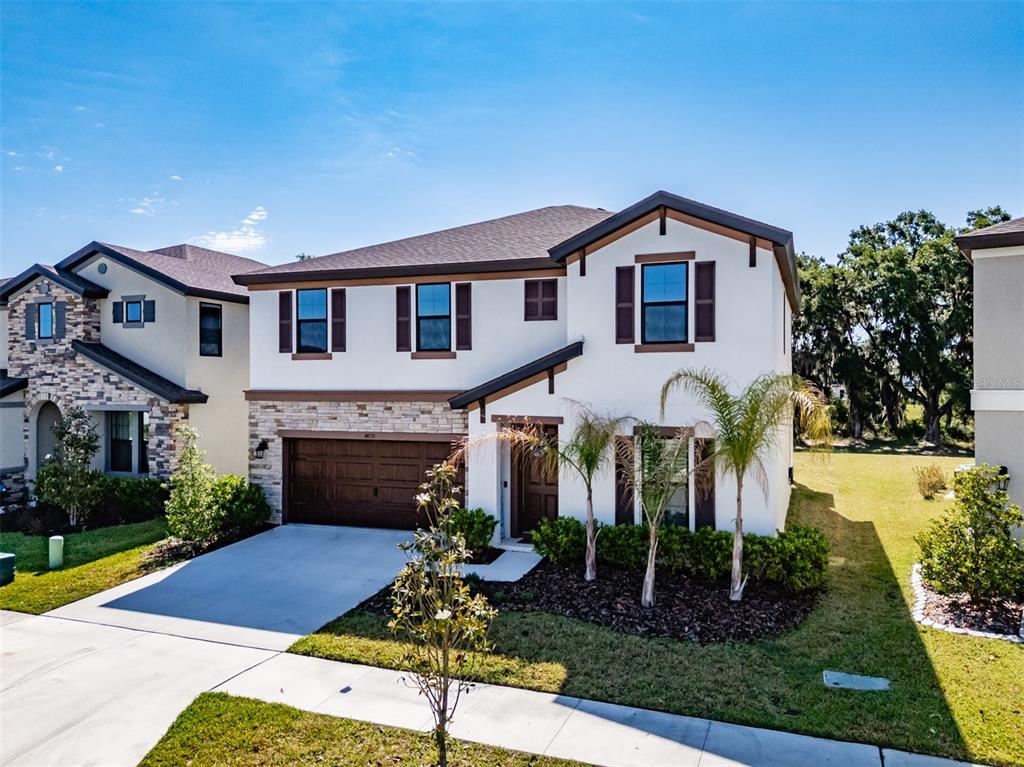 A two-story suburban house with a stucco exterior, stone accents, and a two-car garage — 14733 GALLOP RUN DRIVE, LITHIA, FL