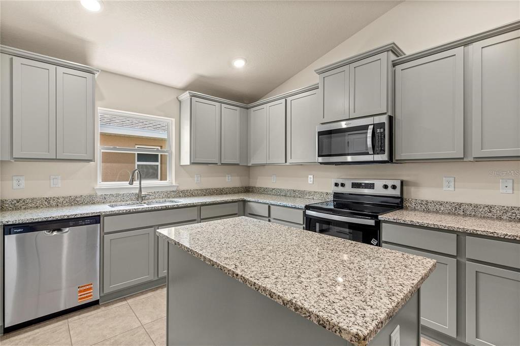 A dining area with a chandelier leads to a kitchen with gray cabinets and carpeted floors — 1667 ANN ROSE WAY, LEESBURG, FL