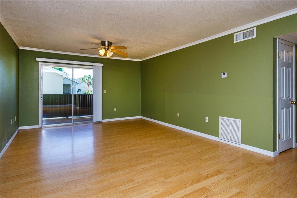 An empty living room features olive green walls, light wood flooring, and a sliding glass door — 908 LAKE DESTINY ROAD UNIT E, ALTAMONTE SPRINGS, FL